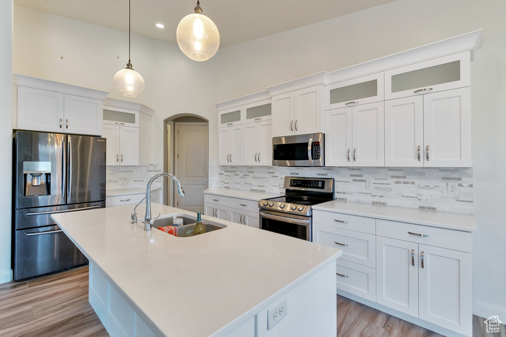 Kitchen with pendant lighting, stainless steel appliances, backsplash, sink, and a kitchen island with sink
