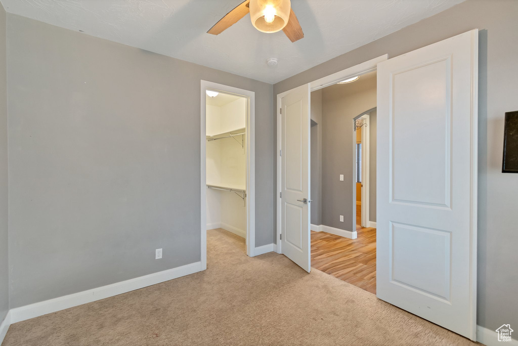 Unfurnished bedroom featuring a closet, ceiling fan, a walk in closet, and light colored carpet