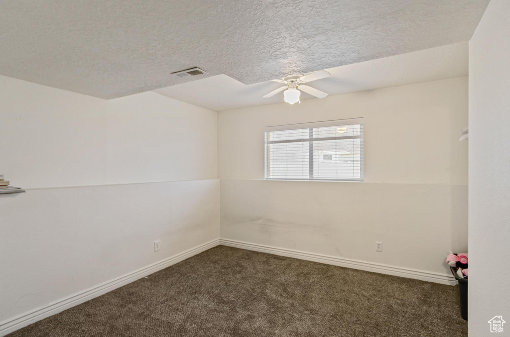 Empty room featuring dark colored carpet, a textured ceiling, and ceiling fan