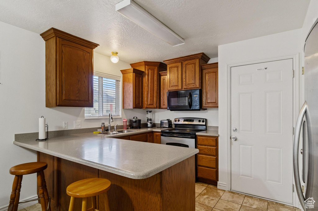 Kitchen with a breakfast bar, stainless steel appliances, sink, light tile floors, and kitchen peninsula