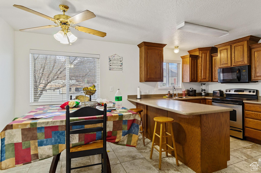 Kitchen with a kitchen breakfast bar, light tile flooring, electric stove, and ceiling fan