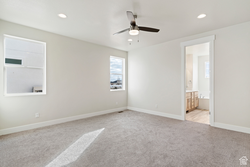 Unfurnished bedroom with light carpet, ensuite bathroom, and ceiling fan