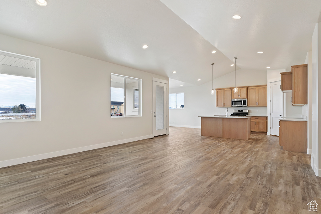 Kitchen featuring a center island with sink, hanging light fixtures, appliances with stainless steel finishes, and hardwood / wood-style flooring