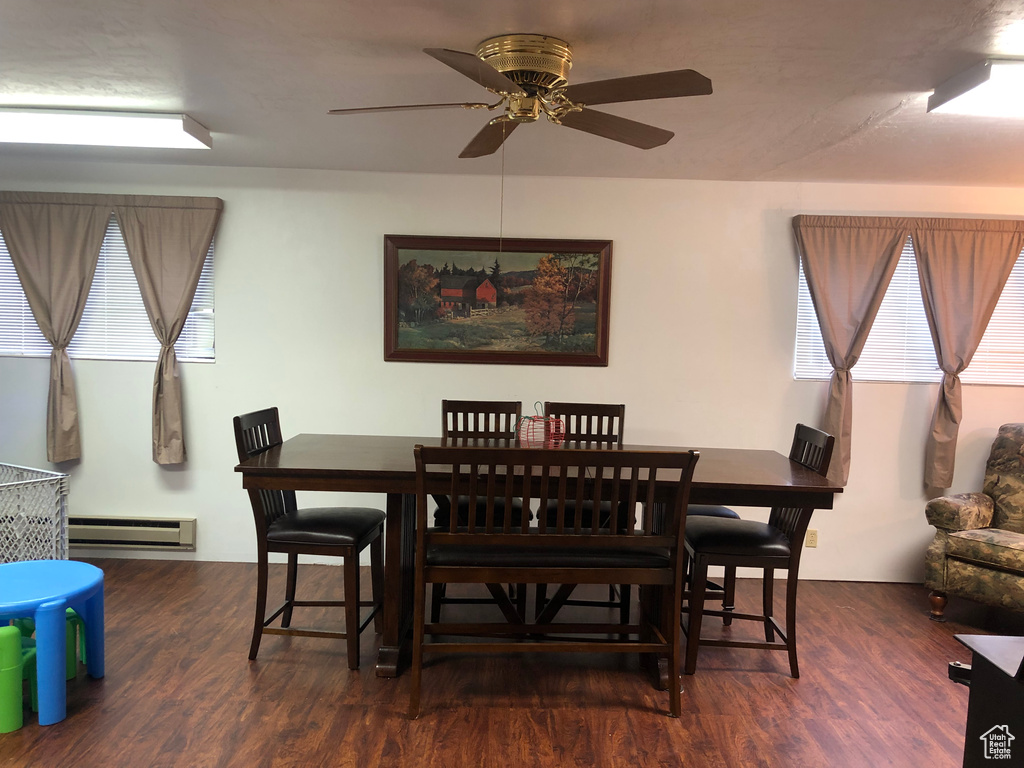 Dining room with ceiling fan, a baseboard heating unit, and dark wood-type flooring