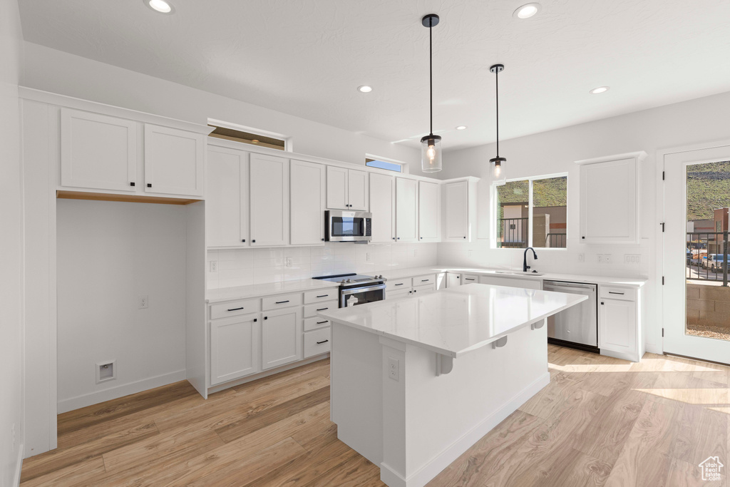 Kitchen with light wood-type flooring, a center island, hanging light fixtures, tasteful backsplash, and appliances with stainless steel finishes