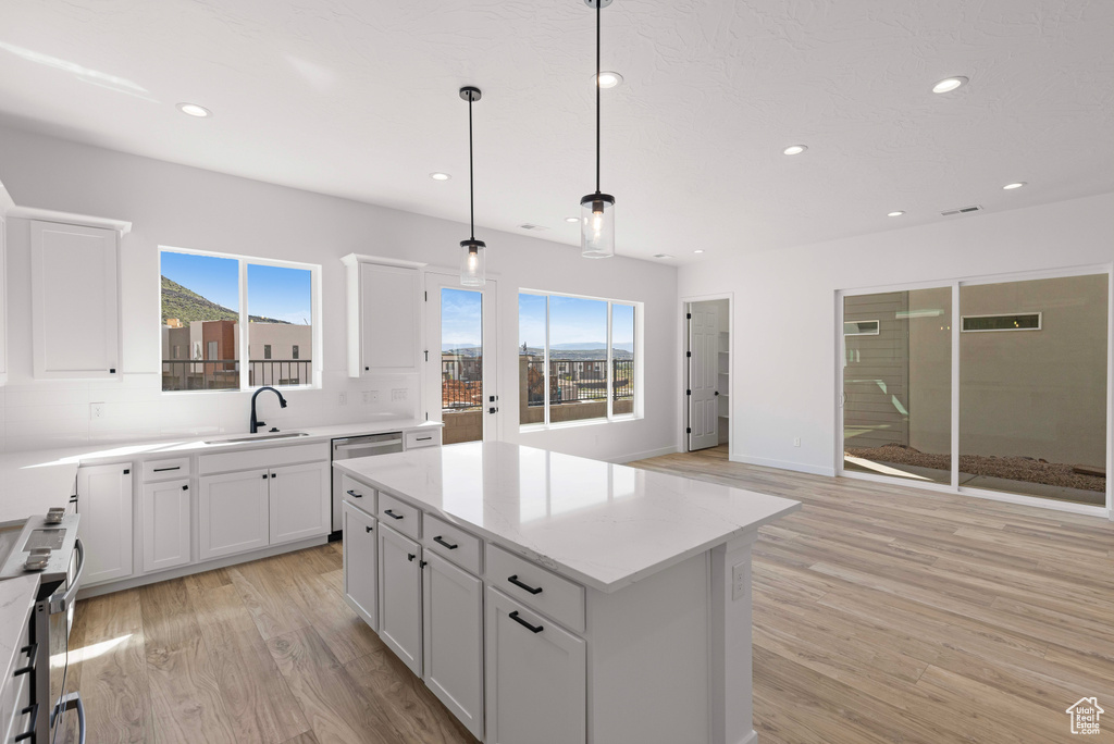 Kitchen with pendant lighting, appliances with stainless steel finishes, white cabinets, a kitchen island, and light wood-type flooring