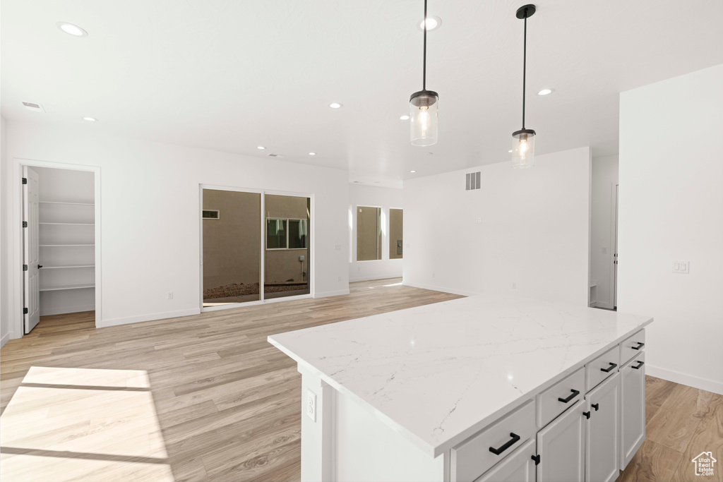 Kitchen featuring decorative light fixtures, a kitchen island, light hardwood / wood-style floors, and white cabinetry