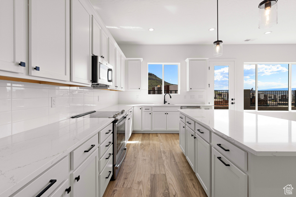 Kitchen with white cabinets, appliances with stainless steel finishes, light hardwood / wood-style floors, and a healthy amount of sunlight