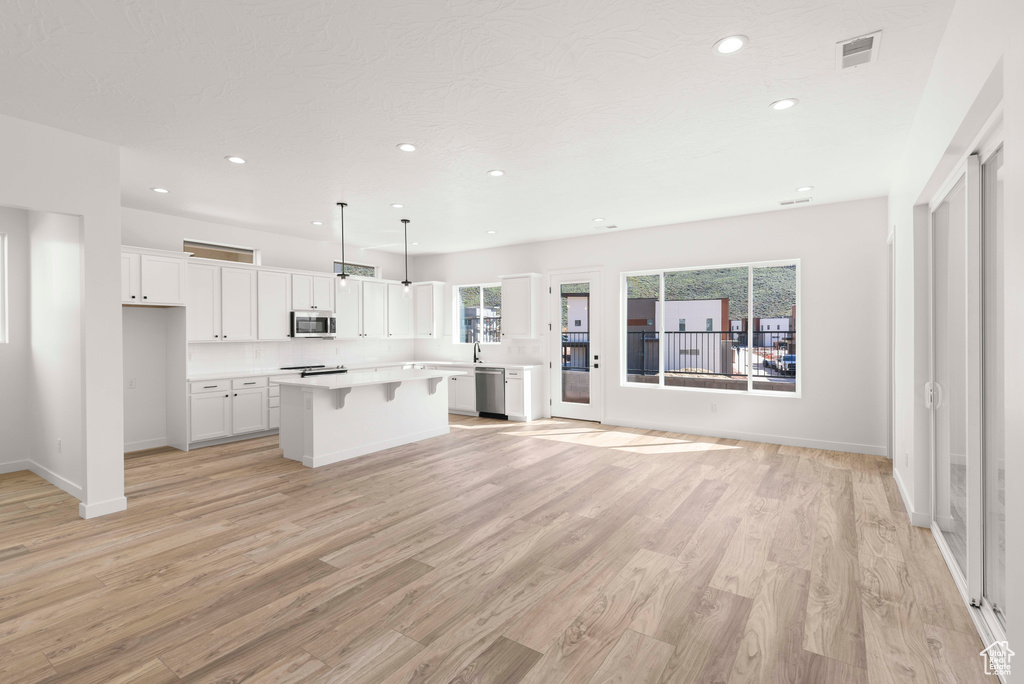 Kitchen featuring white cabinets, appliances with stainless steel finishes, a kitchen island, and light hardwood / wood-style flooring