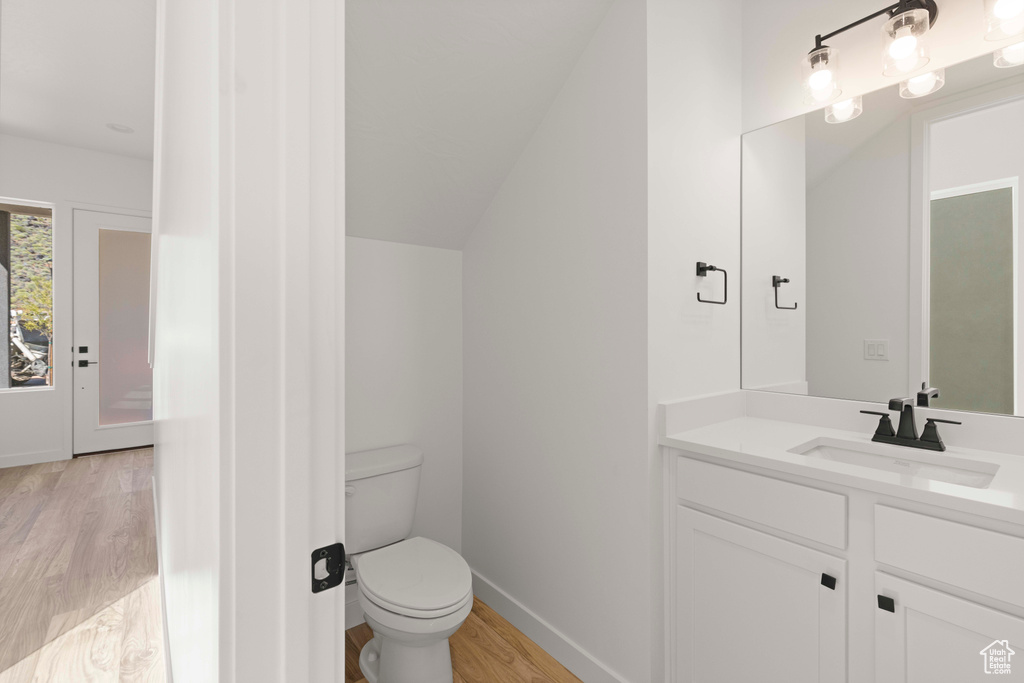 Bathroom with wood-type flooring, vaulted ceiling, vanity, and toilet