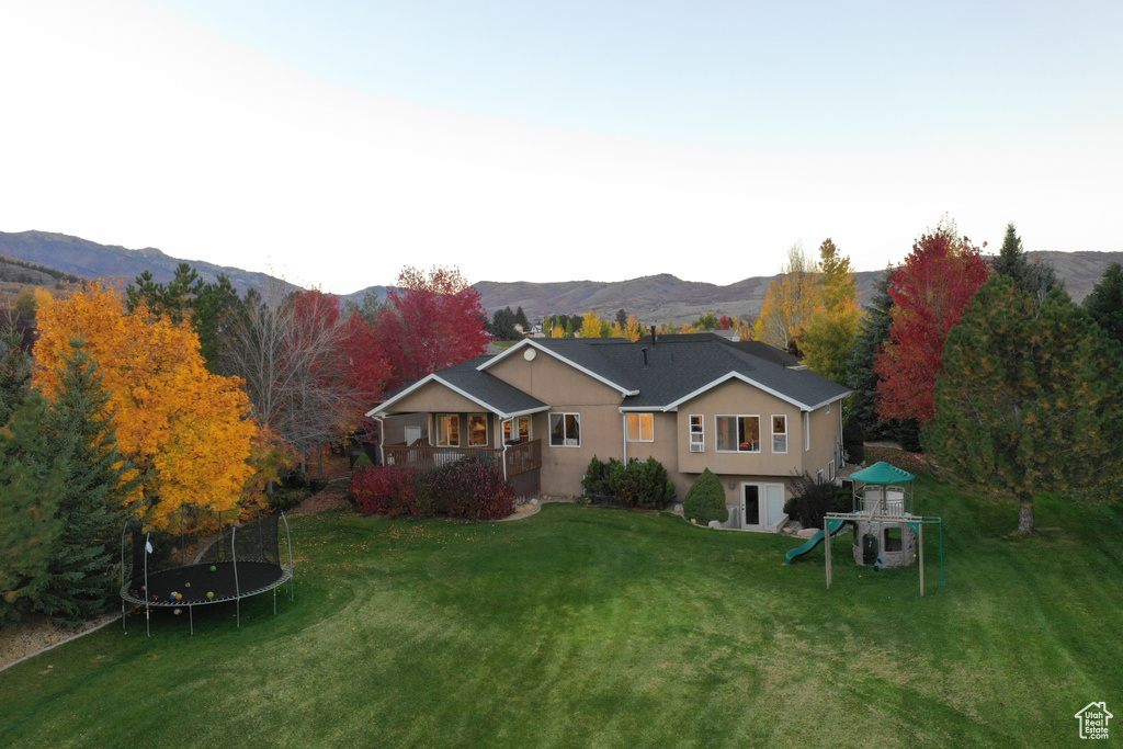 Back of property featuring a playground, a yard, a mountain view, and a trampoline