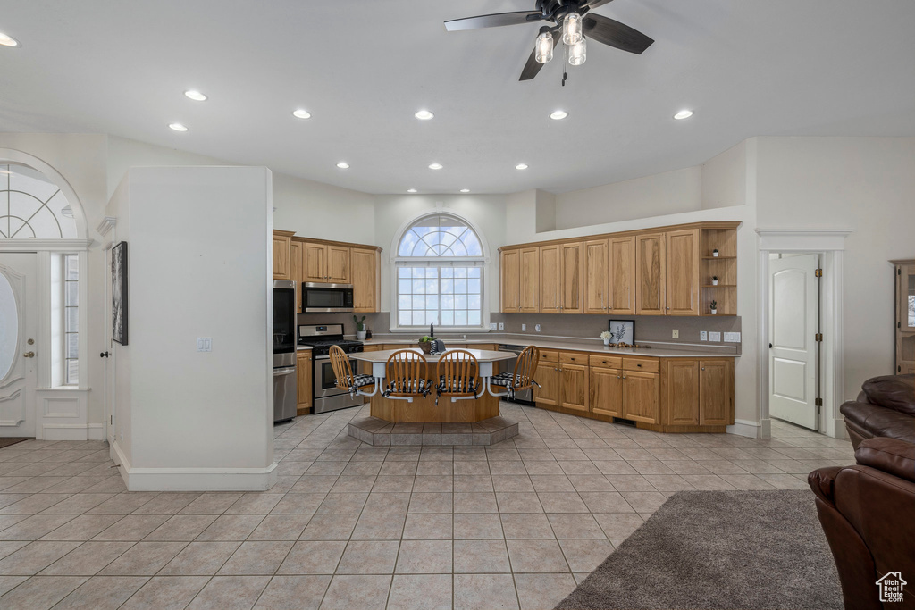 Kitchen with a kitchen breakfast bar, a center island, ceiling fan, light tile floors, and appliances with stainless steel finishes
