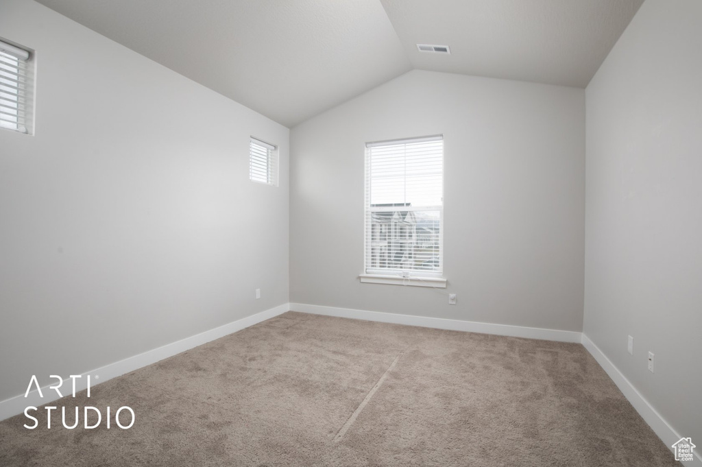 Empty room with vaulted ceiling and light colored carpet