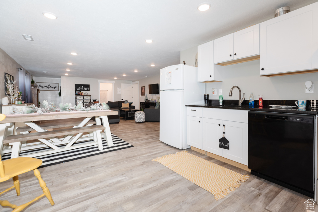 Kitchen with white cabinets, black dishwasher, light wood-type flooring, and white fridge