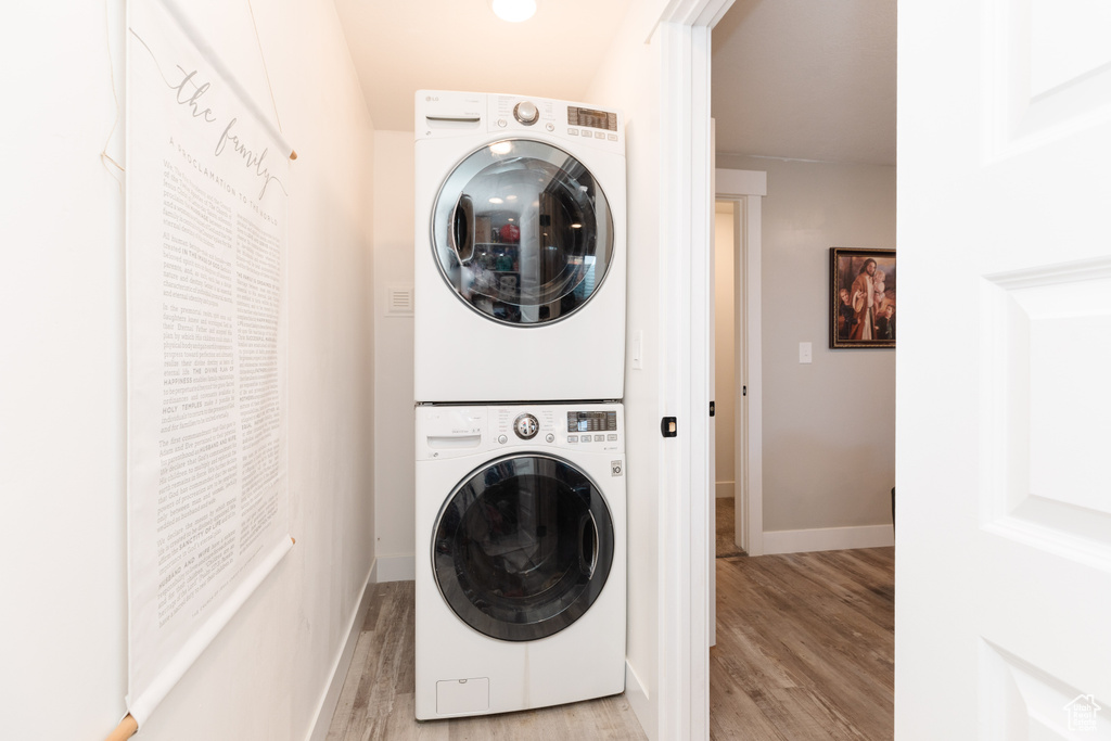 Clothes washing area with light hardwood / wood-style floors and stacked washer and clothes dryer
