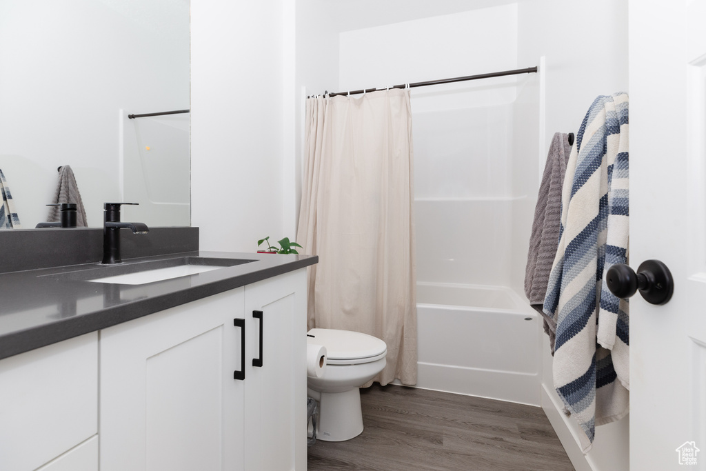 Full bathroom with vanity with extensive cabinet space, shower / tub combo, toilet, and hardwood / wood-style floors