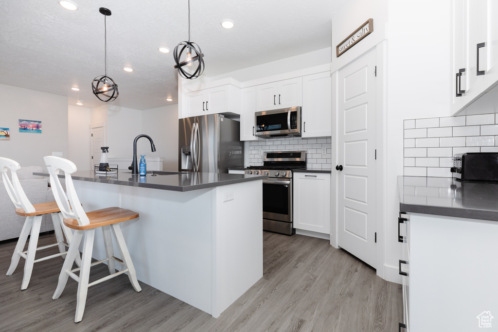 Kitchen with appliances with stainless steel finishes, backsplash, light hardwood / wood-style floors, white cabinets, and a kitchen breakfast bar