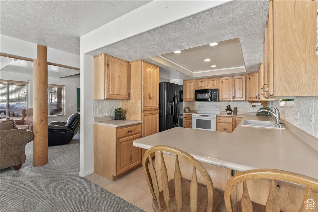 Kitchen featuring a tray ceiling, kitchen peninsula, sink, black appliances, and light colored carpet