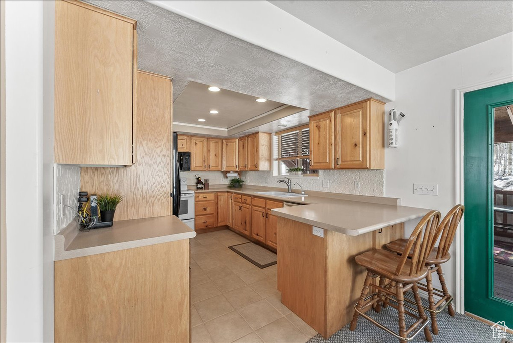 Kitchen with a kitchen breakfast bar, white electric range oven, sink, kitchen peninsula, and light tile flooring