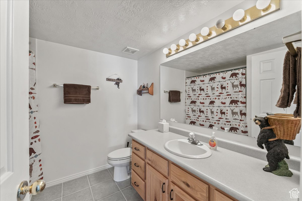 Bathroom with toilet, a textured ceiling, vanity with extensive cabinet space, and tile floors