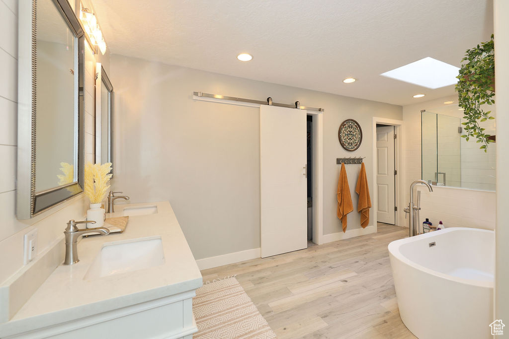 Bathroom with wood-type flooring, dual sinks, a bathing tub, and large vanity