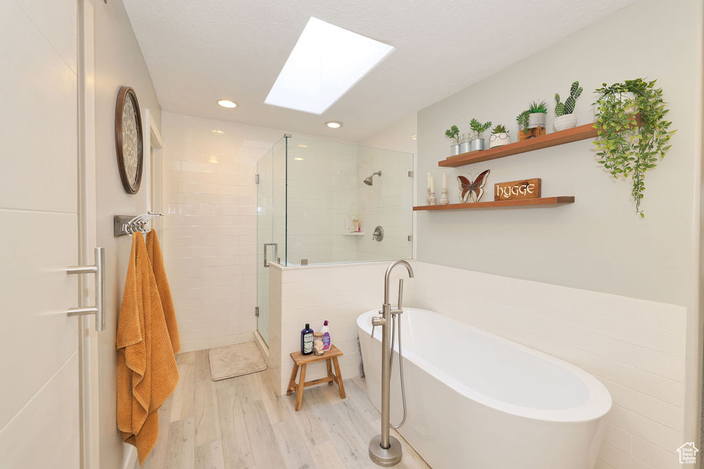 Bathroom with a skylight, independent shower and bath, tile walls, and hardwood / wood-style flooring