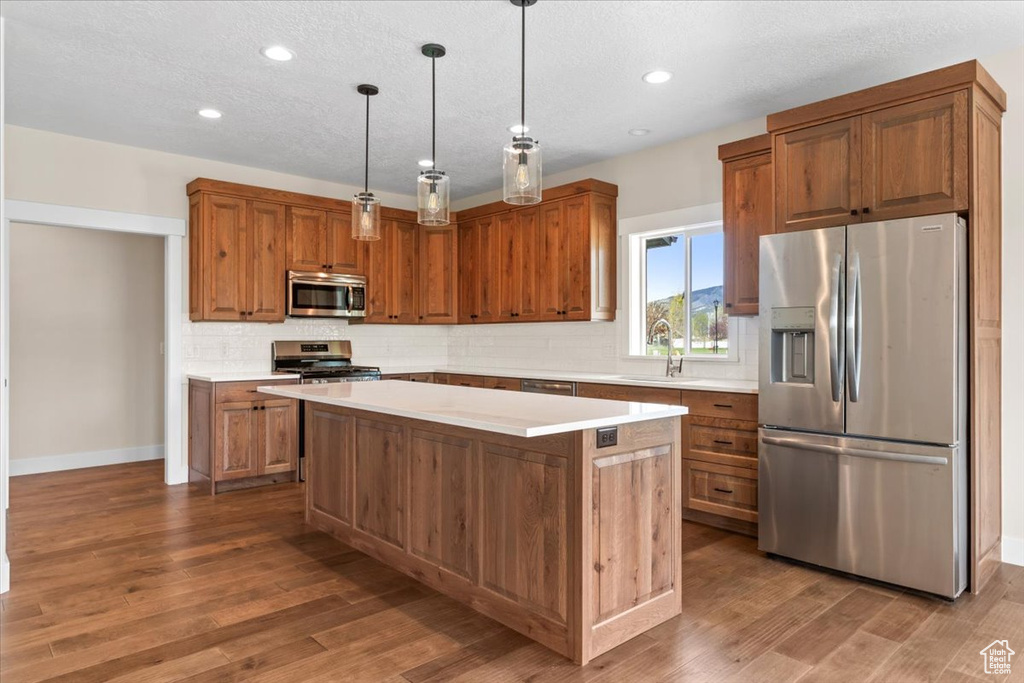 Kitchen with a center island, pendant lighting, stainless steel appliances, sink, and hardwood / wood-style flooring