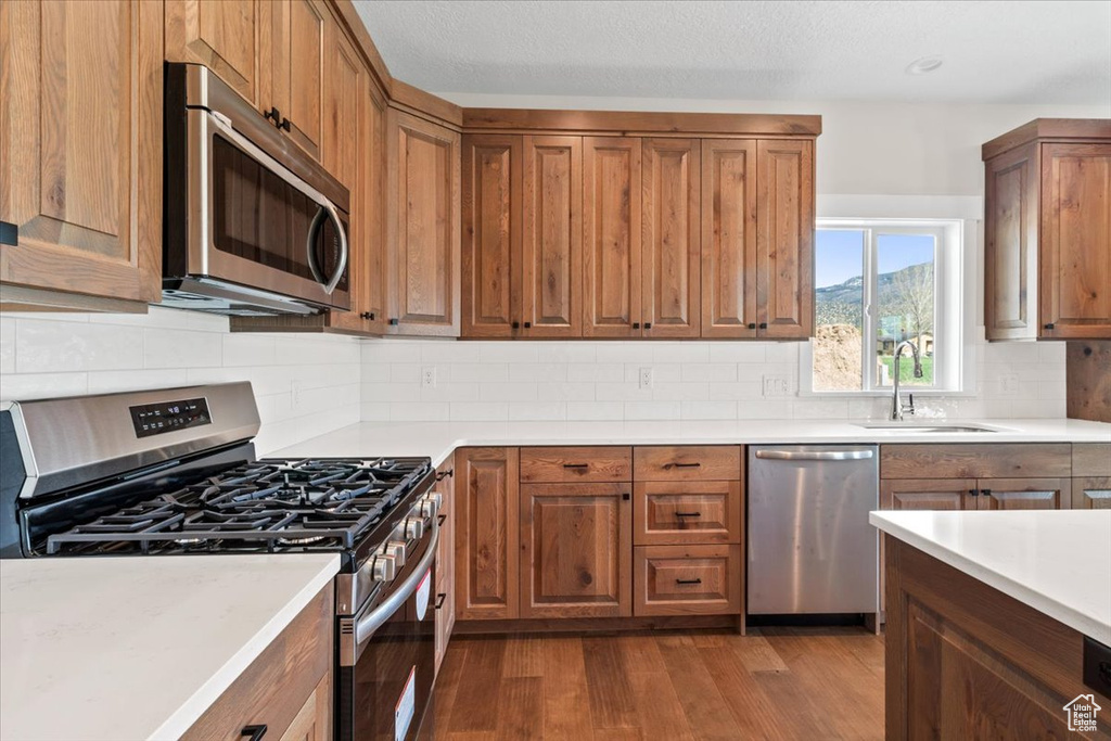 Kitchen featuring wood-type flooring, sink, stainless steel appliances, and backsplash