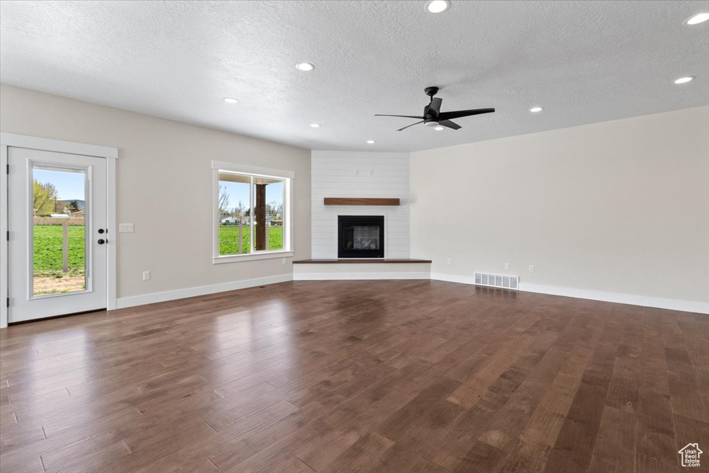 Unfurnished living room featuring a textured ceiling, dark hardwood / wood-style flooring, ceiling fan, and a large fireplace