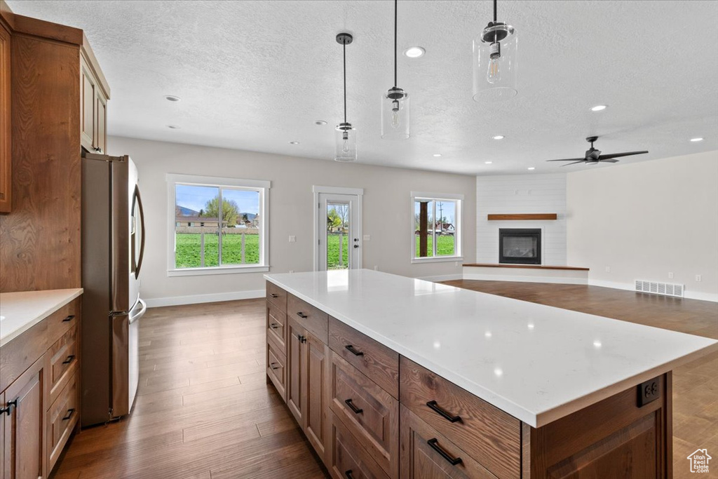 Kitchen featuring a center island, pendant lighting, a large fireplace, stainless steel refrigerator, and hardwood / wood-style floors