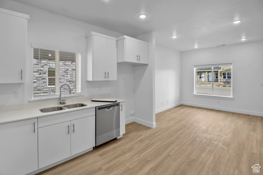 Kitchen with white cabinetry, sink, stainless steel dishwasher, and light hardwood / wood-style floors