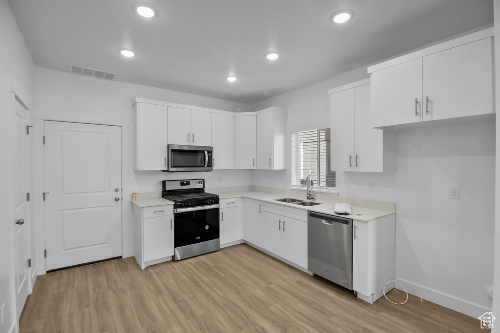 Kitchen featuring light wood-type flooring, appliances with stainless steel finishes, sink, and white cabinetry