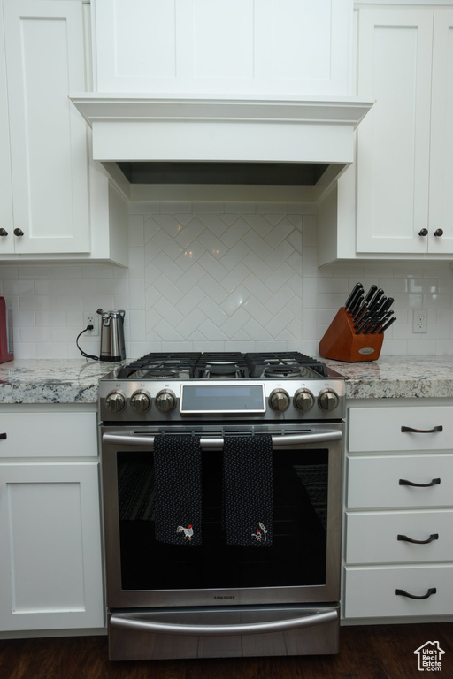Kitchen with backsplash, white cabinets, gas stove, and dark wood-type flooring