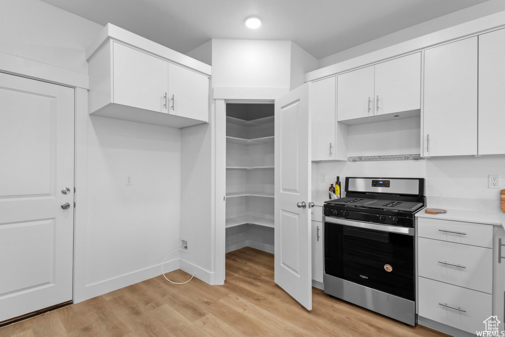 Kitchen with stainless steel gas stove, white cabinets, and light wood-type flooring