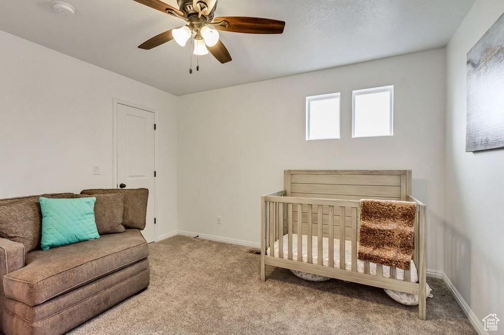 Bedroom featuring light carpet, a crib, and ceiling fan