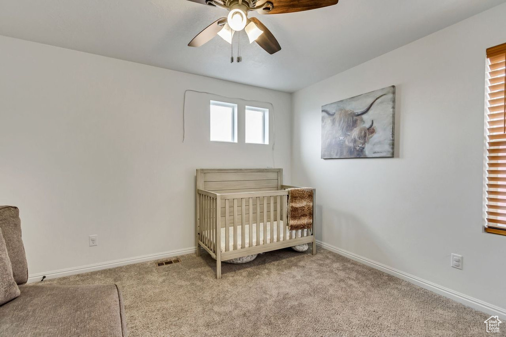 Unfurnished bedroom with ceiling fan, a nursery area, and light colored carpet