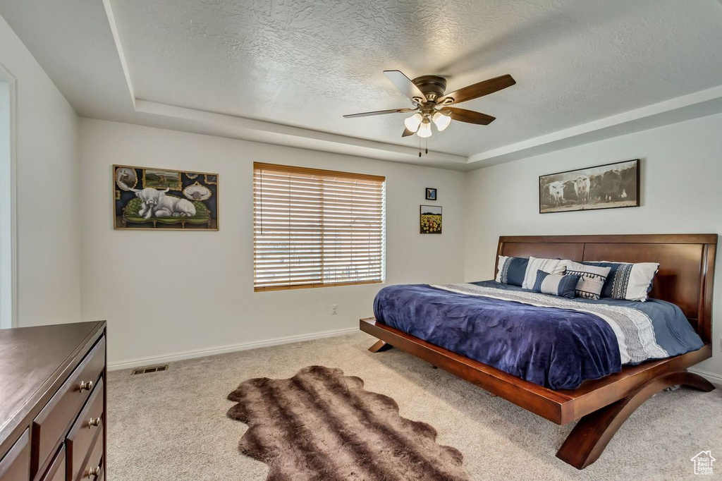 Carpeted bedroom with a textured ceiling, a raised ceiling, and ceiling fan