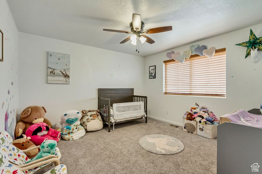 Carpeted bedroom featuring a nursery area and ceiling fan