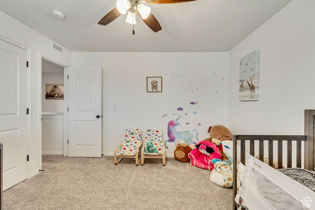 Bedroom with light colored carpet, a nursery area, and ceiling fan