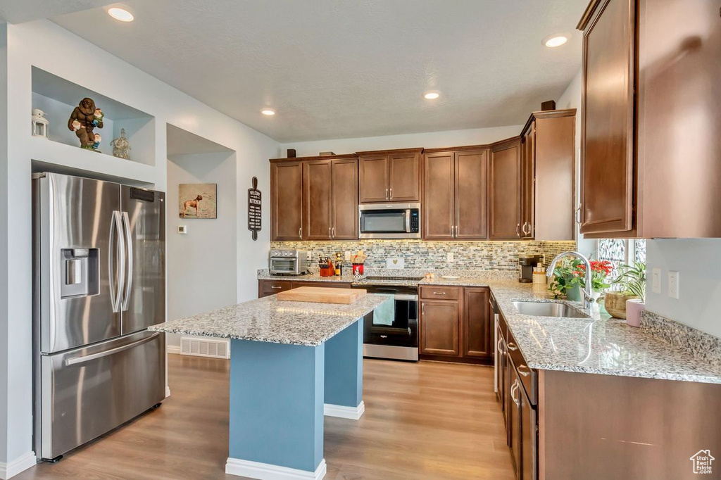 Kitchen featuring light stone countertops, sink, stainless steel appliances, and a center island