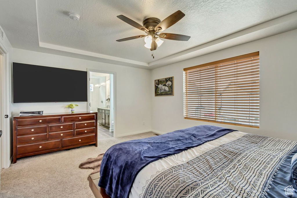 Carpeted bedroom with a raised ceiling, ensuite bath, a textured ceiling, and ceiling fan