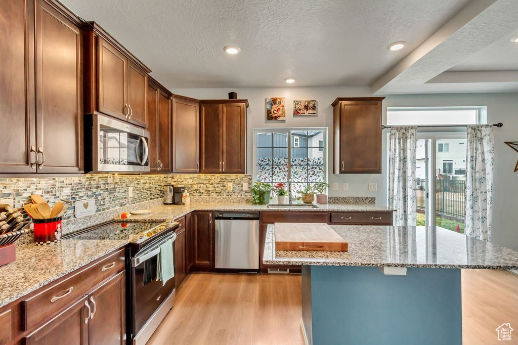 Kitchen featuring light stone counters, sink, stainless steel appliances, and light hardwood / wood-style floors