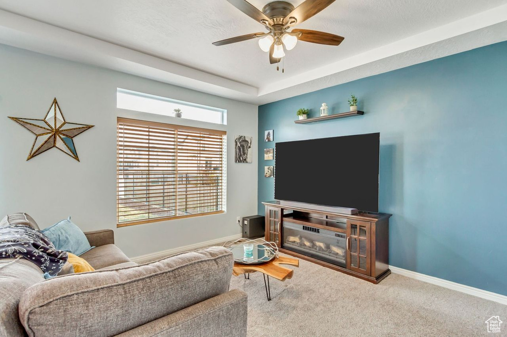 Living room with a raised ceiling, carpet, and ceiling fan