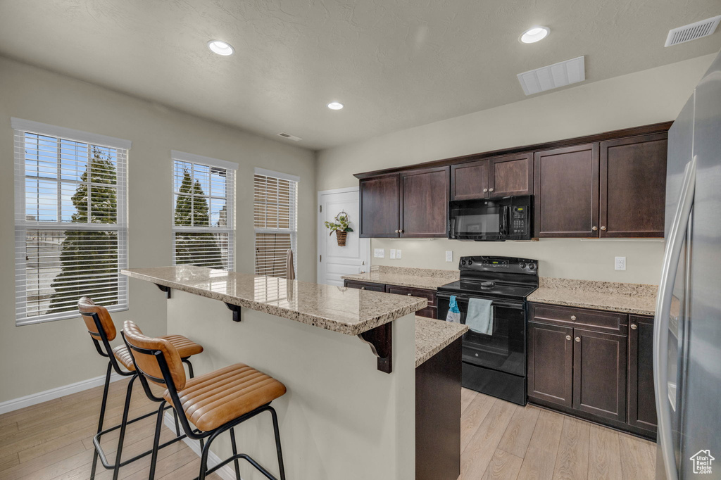 Kitchen with light stone countertops, black appliances, a kitchen breakfast bar, and light hardwood / wood-style floors