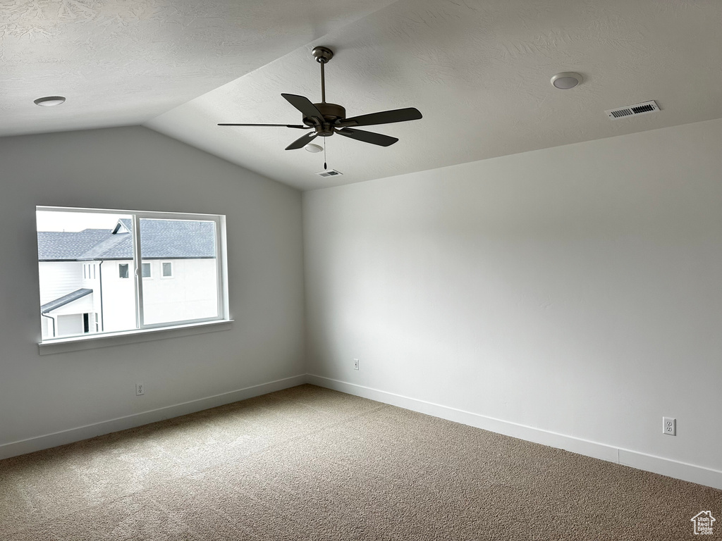 Empty room featuring lofted ceiling, light carpet, and ceiling fan