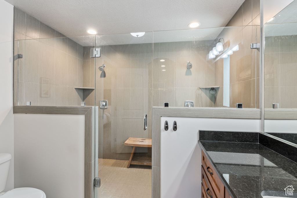 Bathroom featuring a textured ceiling, a shower with door, large vanity, and toilet