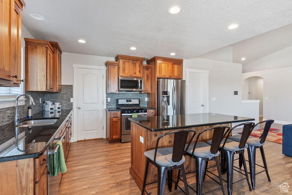 Kitchen featuring backsplash, light hardwood / wood-style floors, a center island, stainless steel appliances, and sink