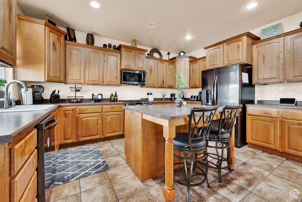 Kitchen featuring a breakfast bar area, black appliances, light tile floors, sink, and a kitchen island