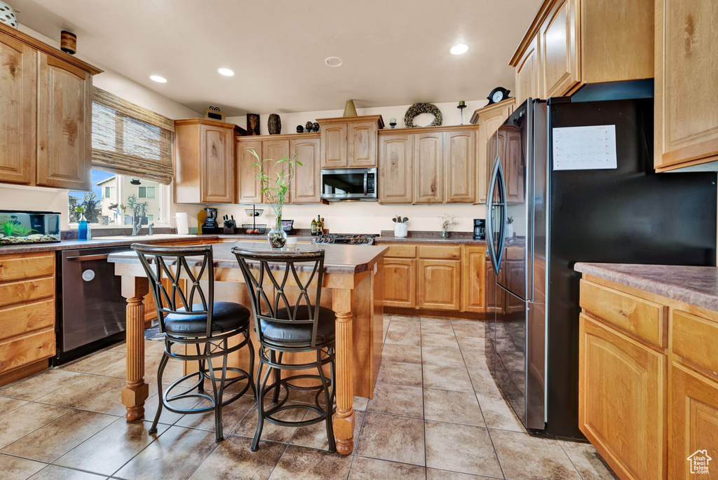 Kitchen with a breakfast bar, a kitchen island, black refrigerator, dishwasher, and light tile floors