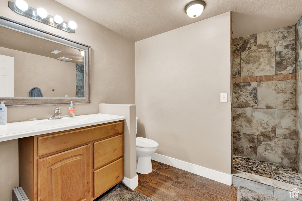Bathroom with vanity, toilet, tiled shower, hardwood / wood-style flooring, and a textured ceiling